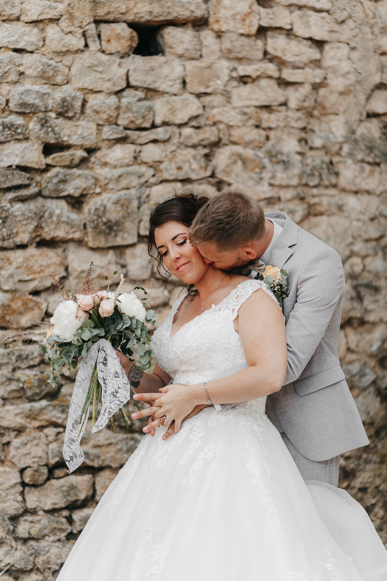 Des mariés s'embrassant devant un mur de pierre, capturés par un photographe mariage Ardennes.