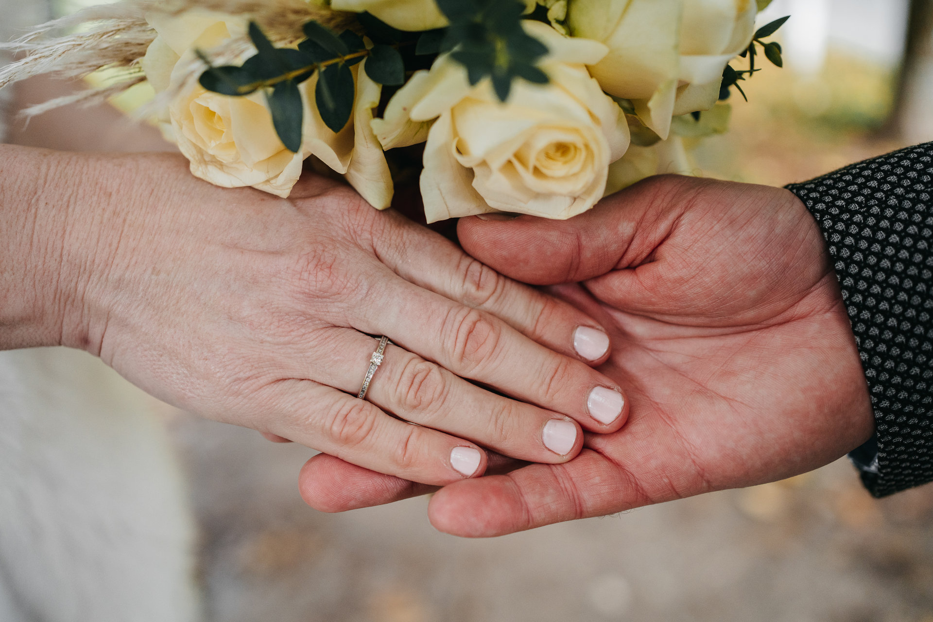 Les mains d'une mariée et d'un marié tenant un bouquet de fleurs.