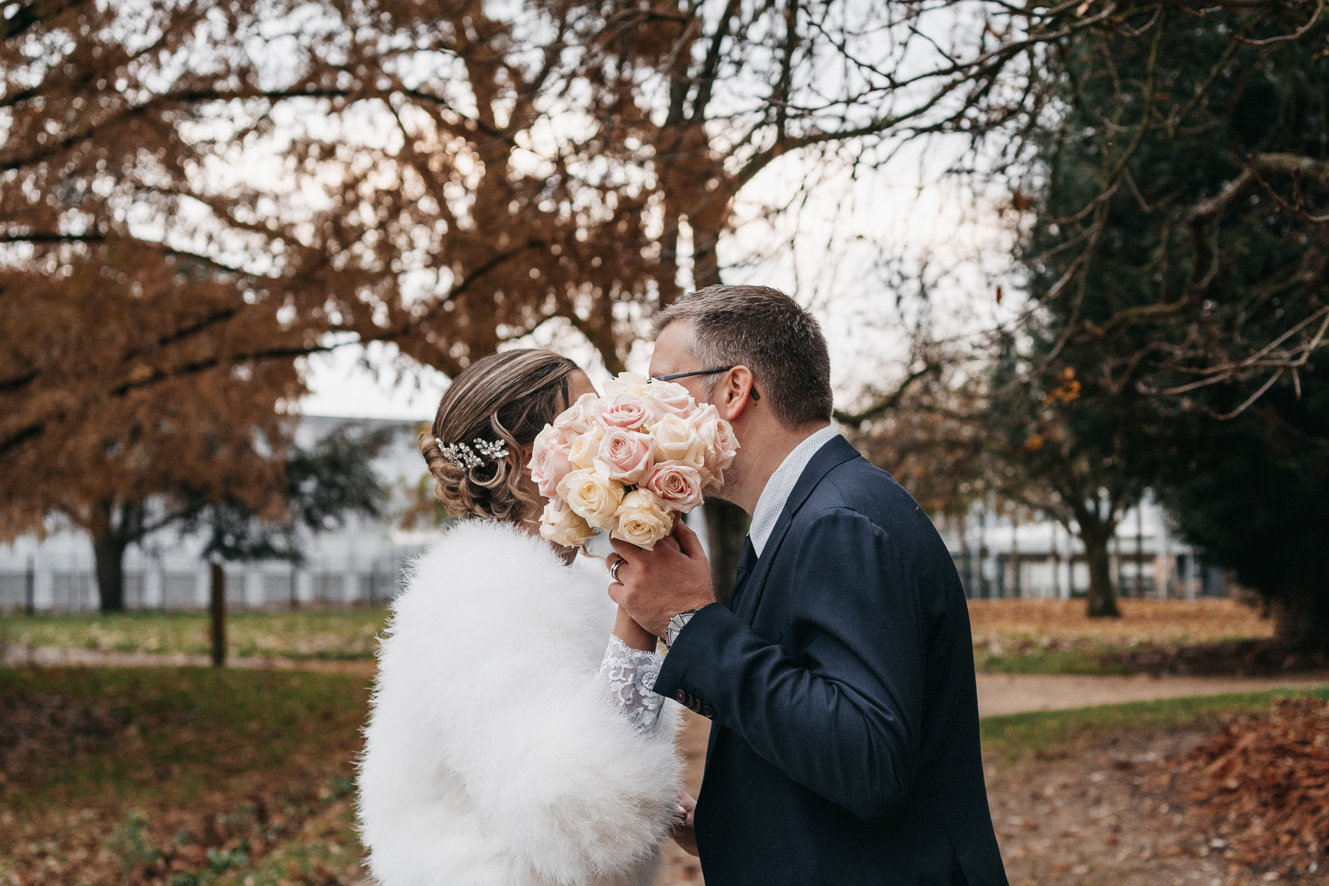 Une mariée et un marié s'embrassant dans un parc.