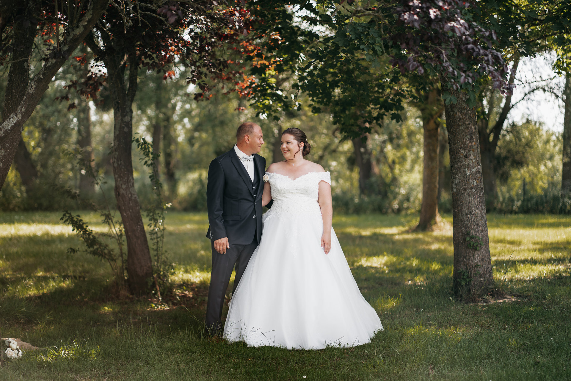 Une mariée et un marié debout sous des arbres dans un champ.