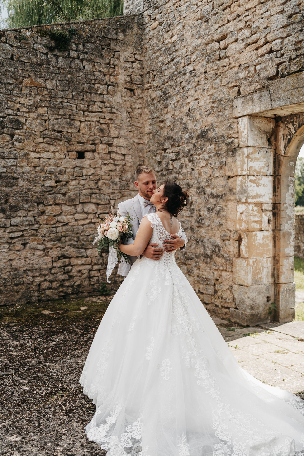 Une mariée et un marié s'embrassent devant un vieux bâtiment en pierre.
