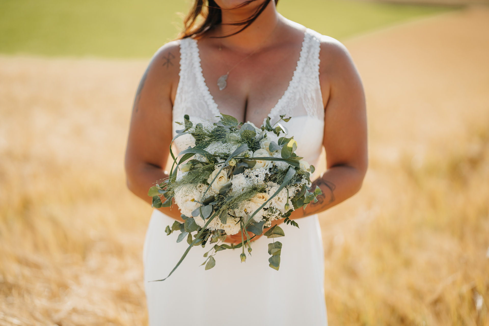 Une mariée tenant un bouquet dans un champ de blé.