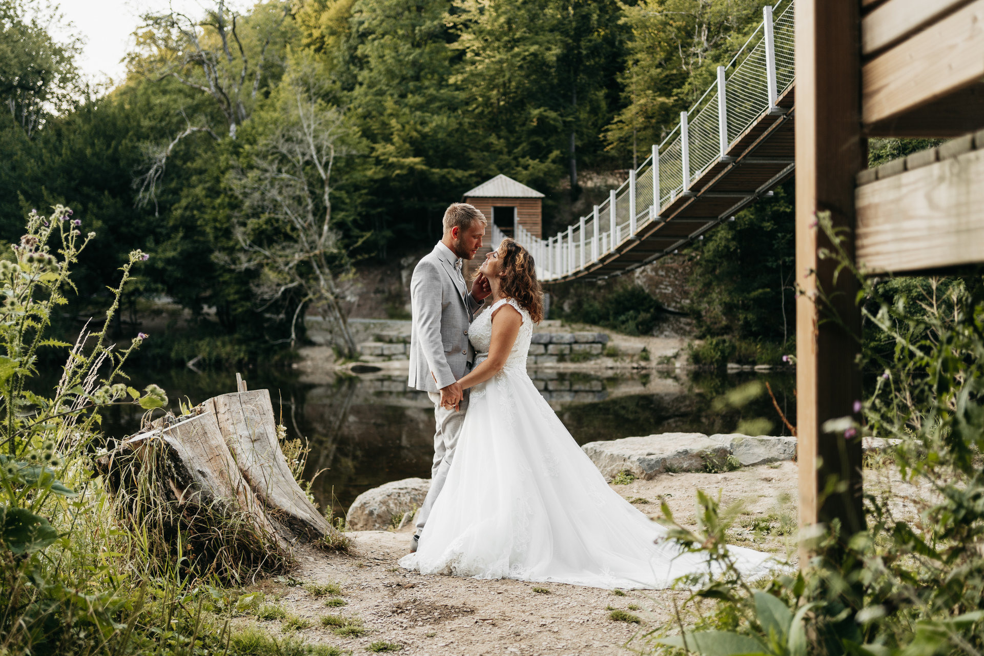Une mariée et un marié debout à côté d'un pont suspendu dans une zone boisée.
