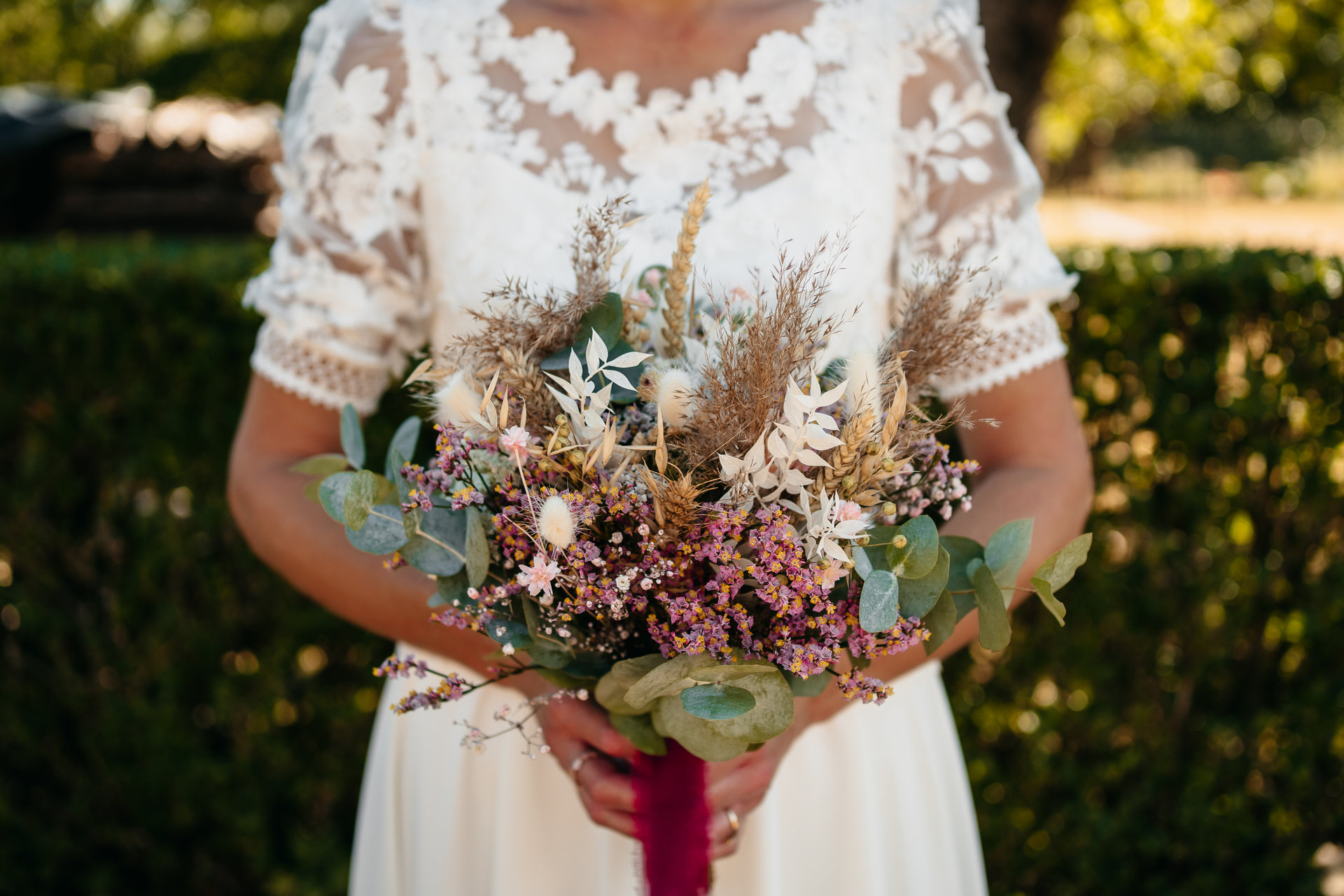 Une mariée tenant un bouquet de fleurs séchées.