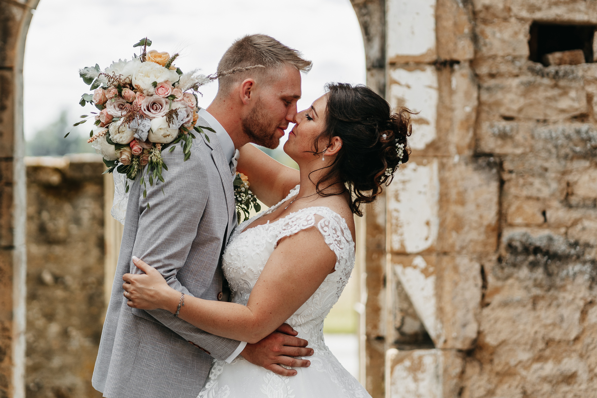 Une mariée et un marié s'embrassant devant une arche de pierre.