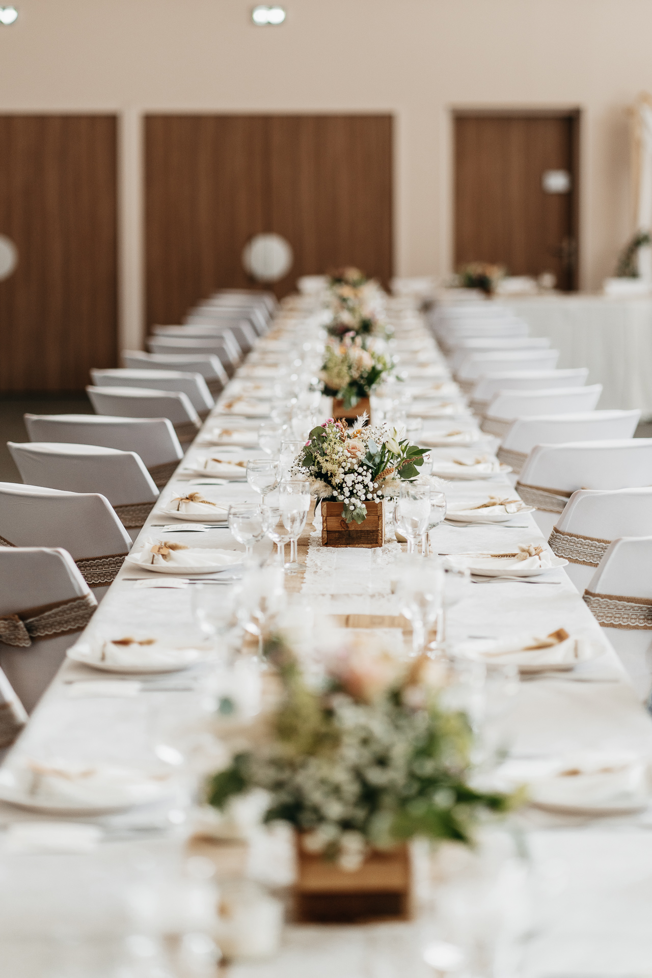 une longue table est dressée avec des assiettes blanches et des fleurs.