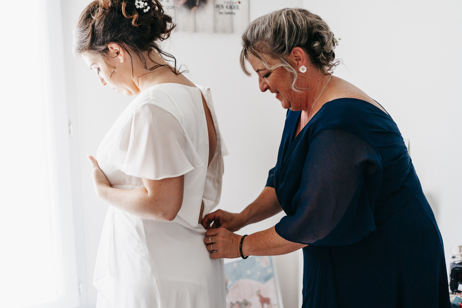 Une mère aide sa fille à mettre sa robe de mariée.
