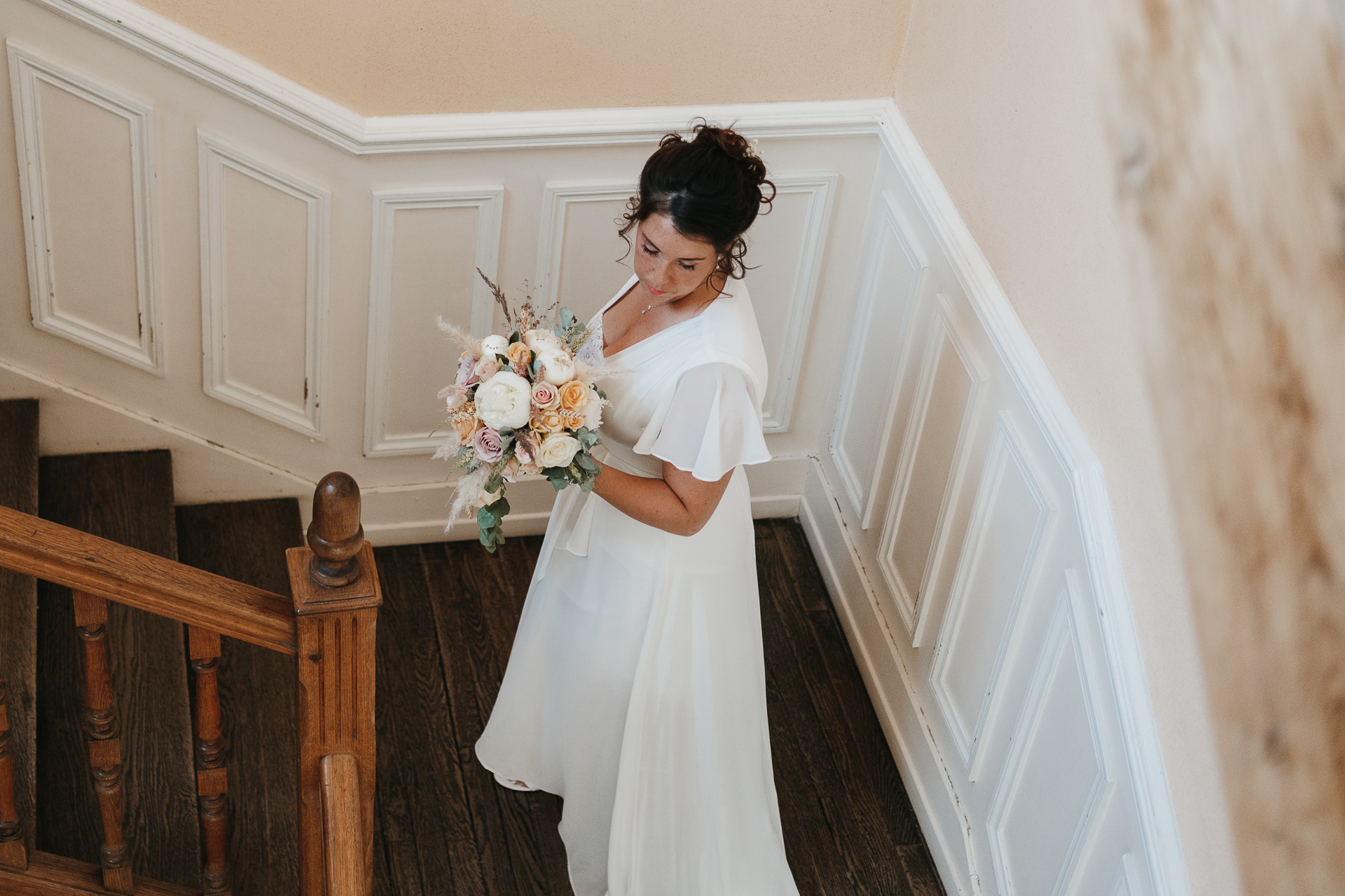 Une mariée en robe blanche debout sur un escalier.
