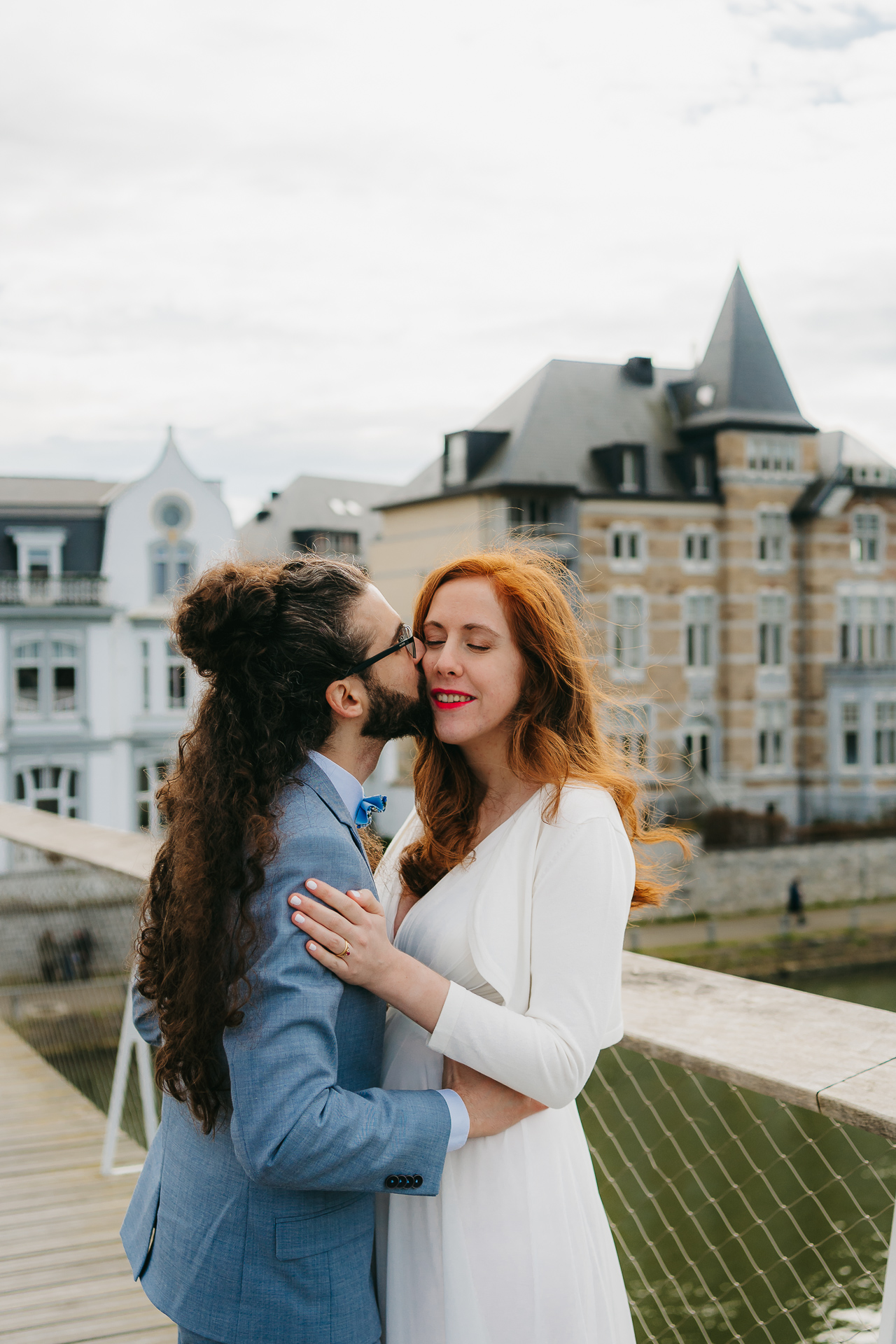 Un couple s'embrassant et partageant un moment sur un pont avec un bâtiment historique en arrière-plan.