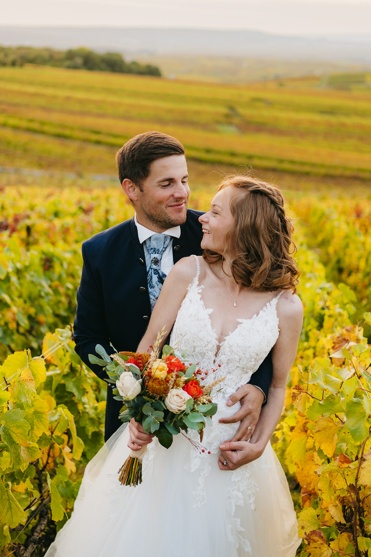 Un couple heureux en tenue de mariage posant dans un vignoble.