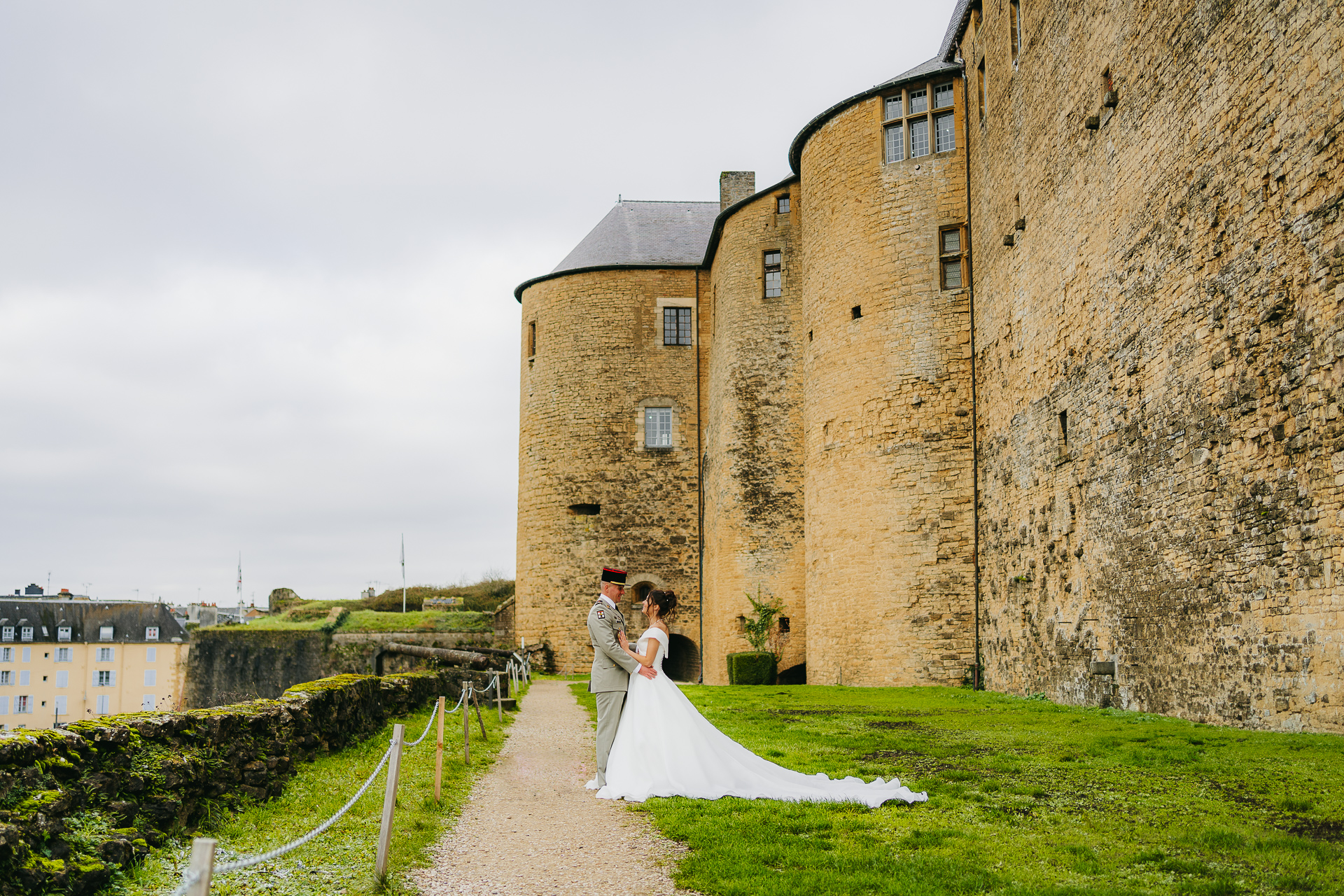 Un couple de jeunes mariés s'embrassant devant un grand château historique en pierre.