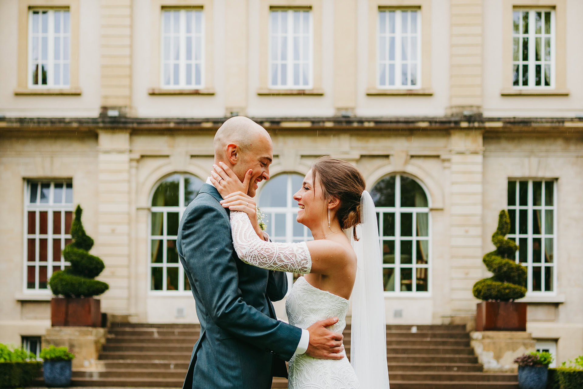 Une mariée et un marié se tiennent devant le Château du Bois d'Arlon, souriant et s'embrassant le jour de leur mariage.